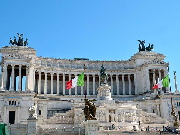 The towering Altare della Patria in Rome glowing golden at sunset, overlooking the Colosseum and Roman Forum.