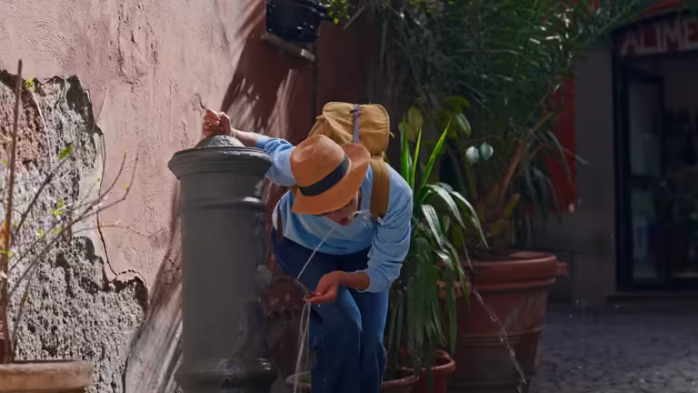 Tourist refilling water bottle at a traditional Rome Nasone fountain in the city center