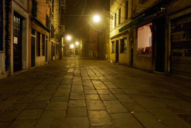 Quiet Venetian street at night with warm lights and empty canals.