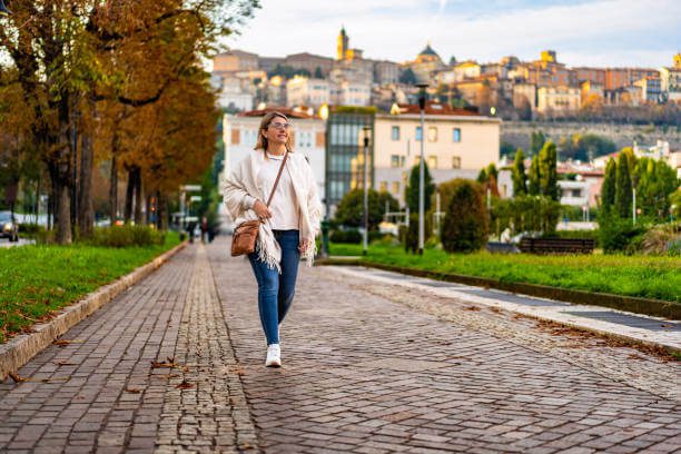 Woman walking a cobblestone street in Italy in October wearing a layered autumn outfit — light sweater, jeans, and ankle boots