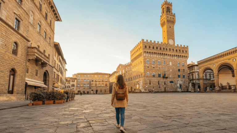 How many days in Florence solo traveler with small daypack walking through Piazza della Signoria in golden morning light with Palazzo Vecchio tower behind