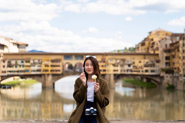 solo traveller eating authentic Florentine gelato walking across Ponte Vecchio bridge in the late afternoon